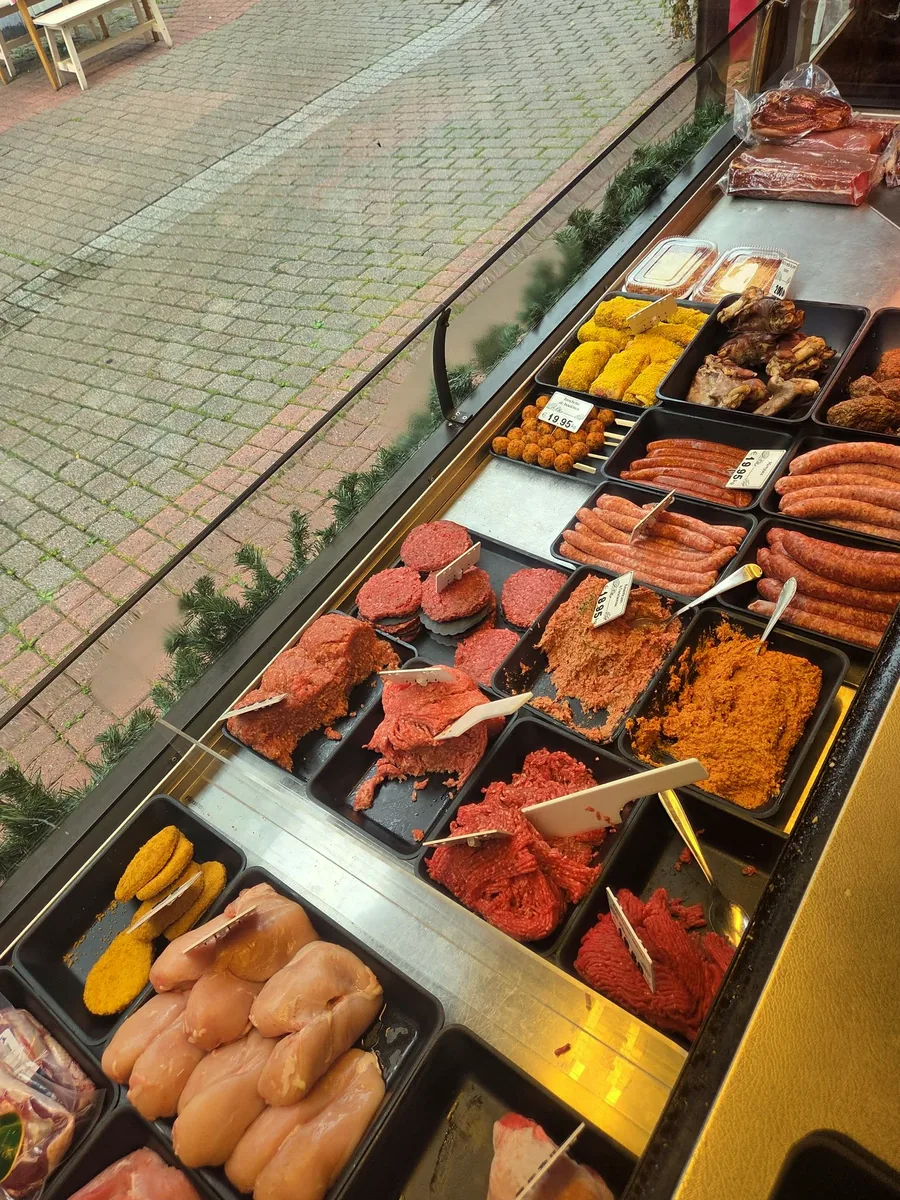 Le comptoir réfrigéré de la Boucherie Léon vu depuis la rue, garni de brochettes, de hachés et de préparations du jour.